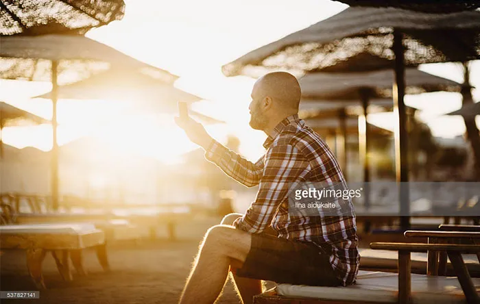 مردی که روی صندلی نشسته و با موبایل سرگرم شده است