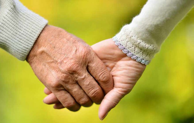 Elderly-couple-holding-hands-over-natural-background-16x9