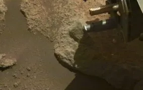 لحظه‌ی پرتاب قطعات سنگ‌ریزه‌ی اضافی از مته‌ی انتهای بازوی رباتیک مریخ‌نورد پشتکارلحظه‌ی پرتاب قطعات سنگ‌ریزه‌ی اضافی از مته‌ی انتهای بازوی رباتیک مریخ‌نورد پشتکار