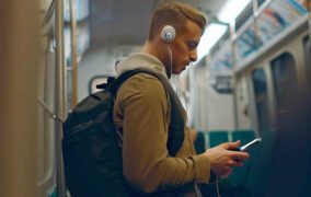 پسری درون واگن مترو با هدفون روی گوش و کوله پشتی، به موبایل خود نگاه می‌کند.