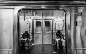 دو نفر در حال مطالعه کتاب در متروی نیویورک هستند