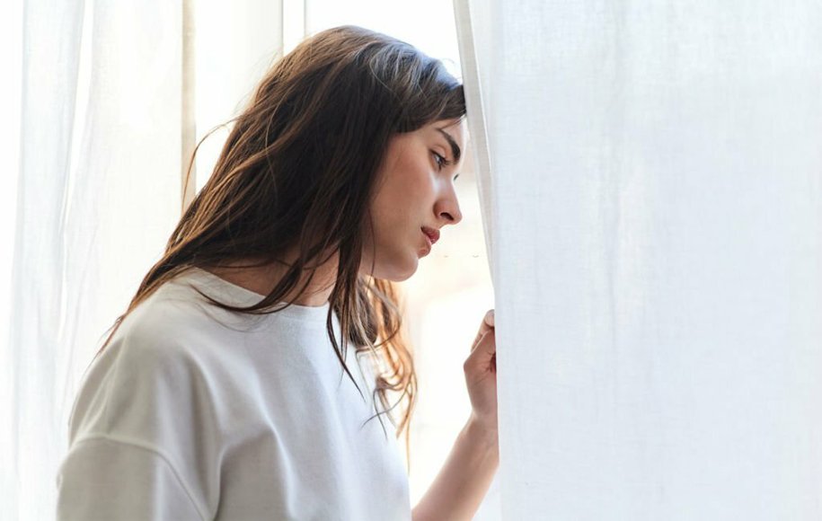 یک زن افسرده که از پنجره به بیرون نگاه می‌کند