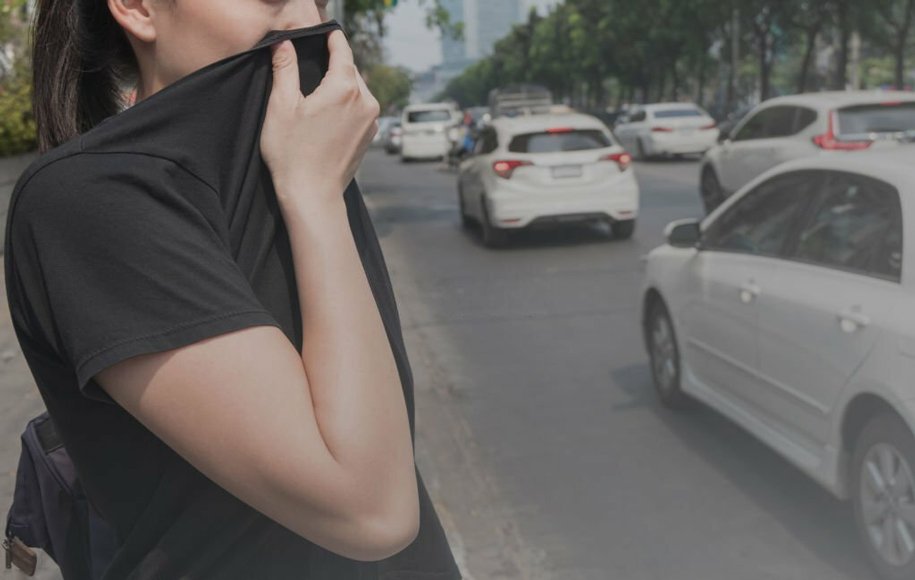 یک زن در کنار خیابان که با یقه لباس جلوی دهان و بینی خود را گرفته است