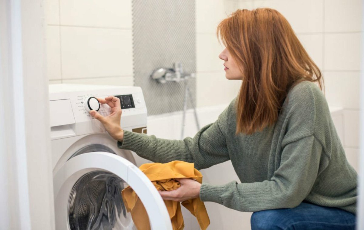 یک زن که لباس‌ها را داخل ماشین لباسشویی می‌گذارد