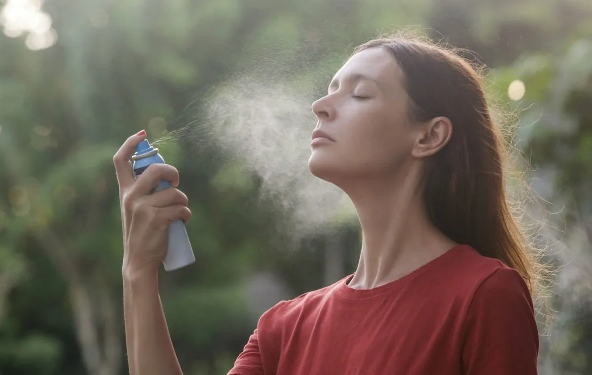 یک زن در طبیعت که فیس میست خانگی را روی صورت خود اسپری می‌کند