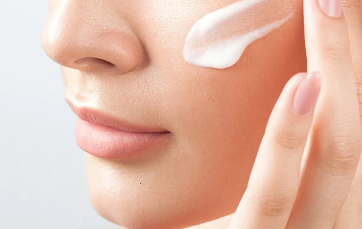 یک زن که کمی کرم روی گونه خود زده است تا از خواص کرم شب اوریفلیم بهرهمند شود