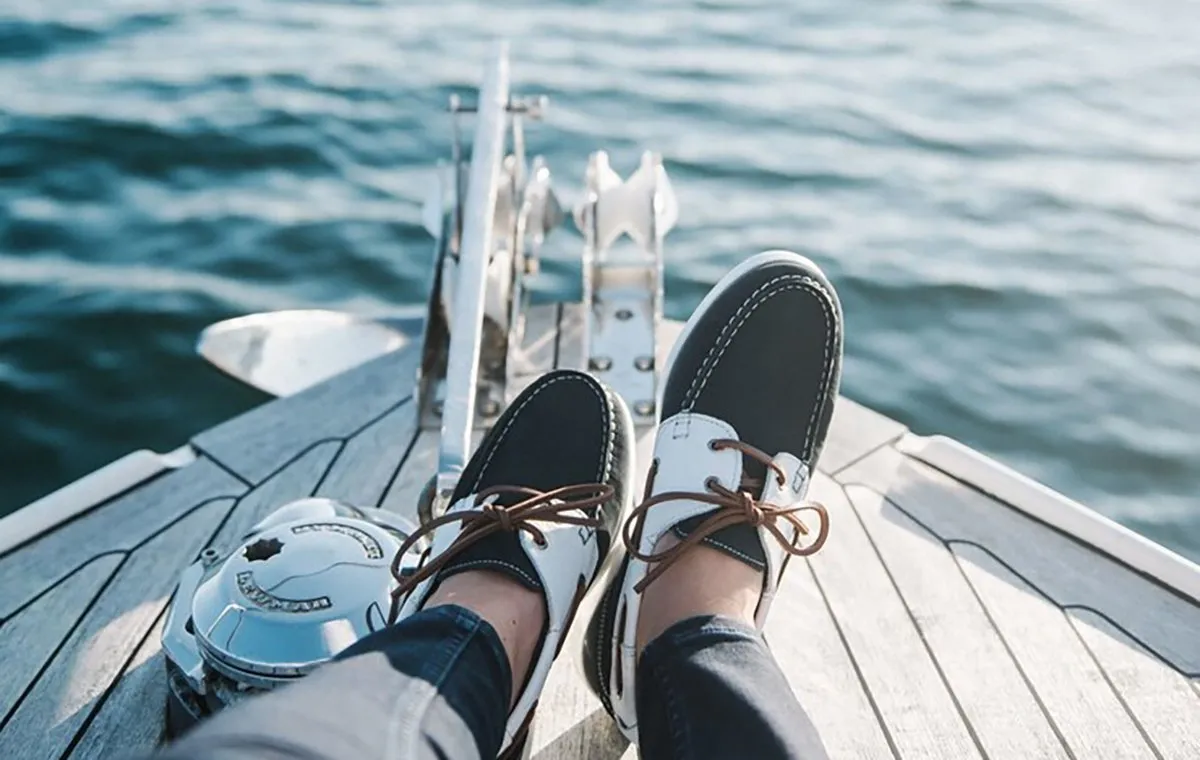 مردی با کفش قایقی روی عرشه‌ی یک قایق تفریحی