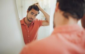 یک مرد که در آینه به موهای خود نگاه می‌کند