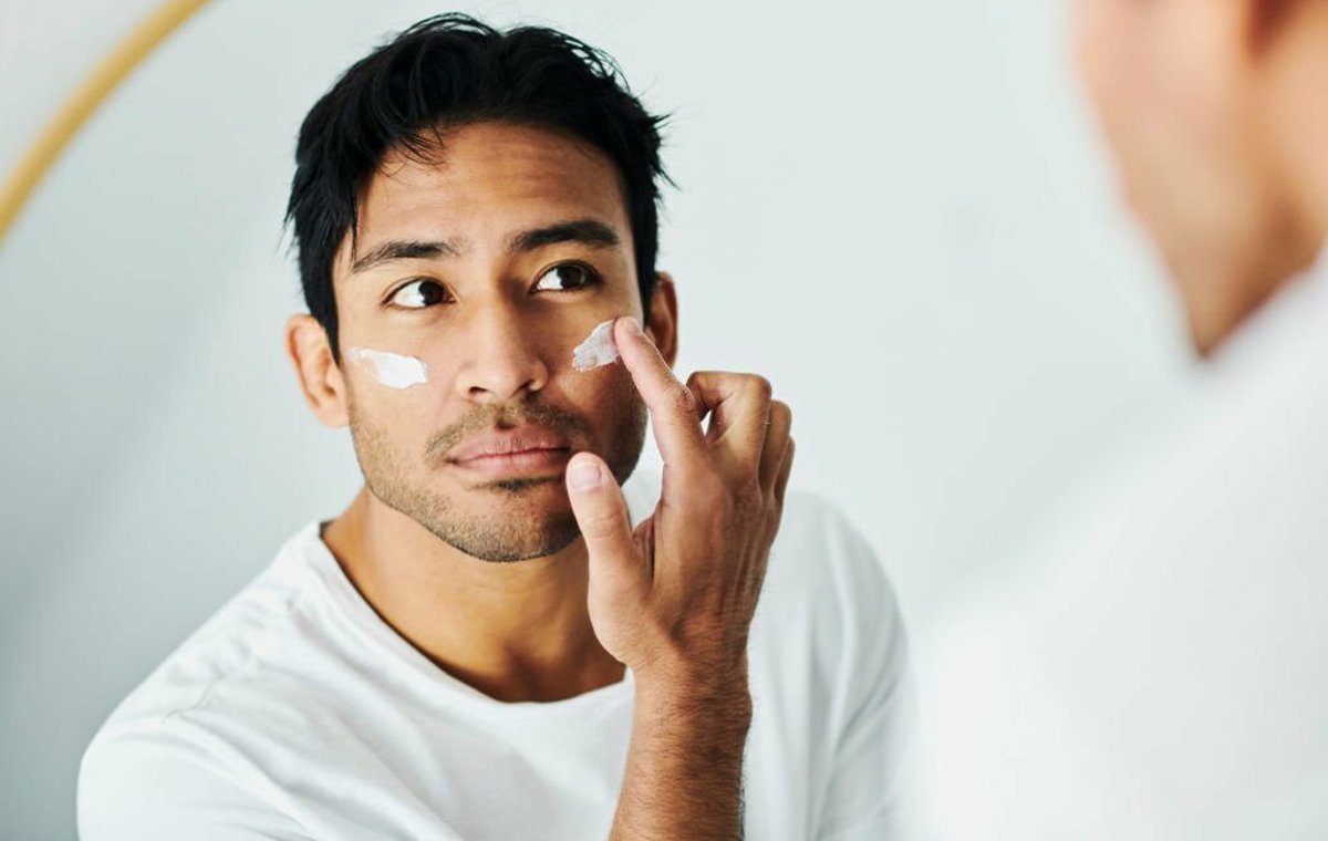 یک مرد در جلوی آینه که بهترین کرم ضد آفتاب برای پوست خشک و جوش دار را به صورتش می‌مالد