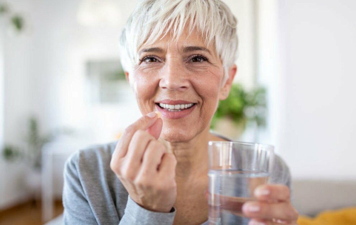 یک زن سالمند که در حال خوردن مکمل با یک لیوان آب است