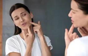 زنی در حال فشار دادن جوش روی صورتش است.