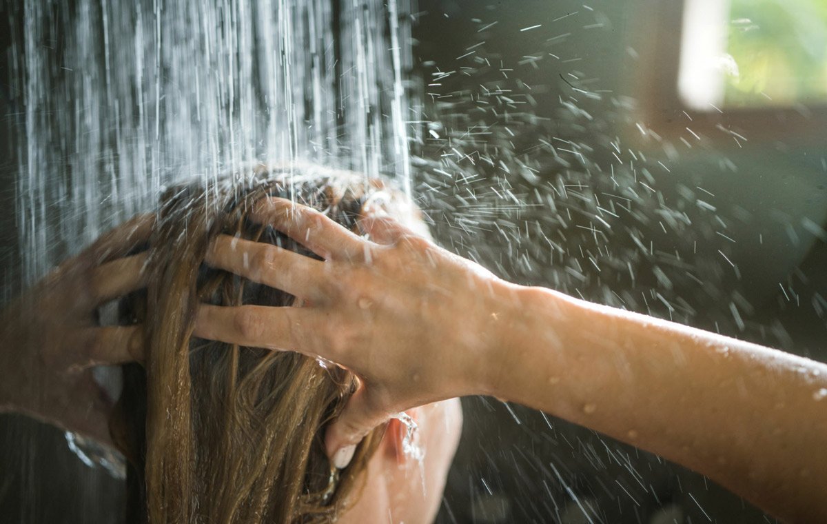 یک زن که زیر دوش موهای خود را می‌شوید