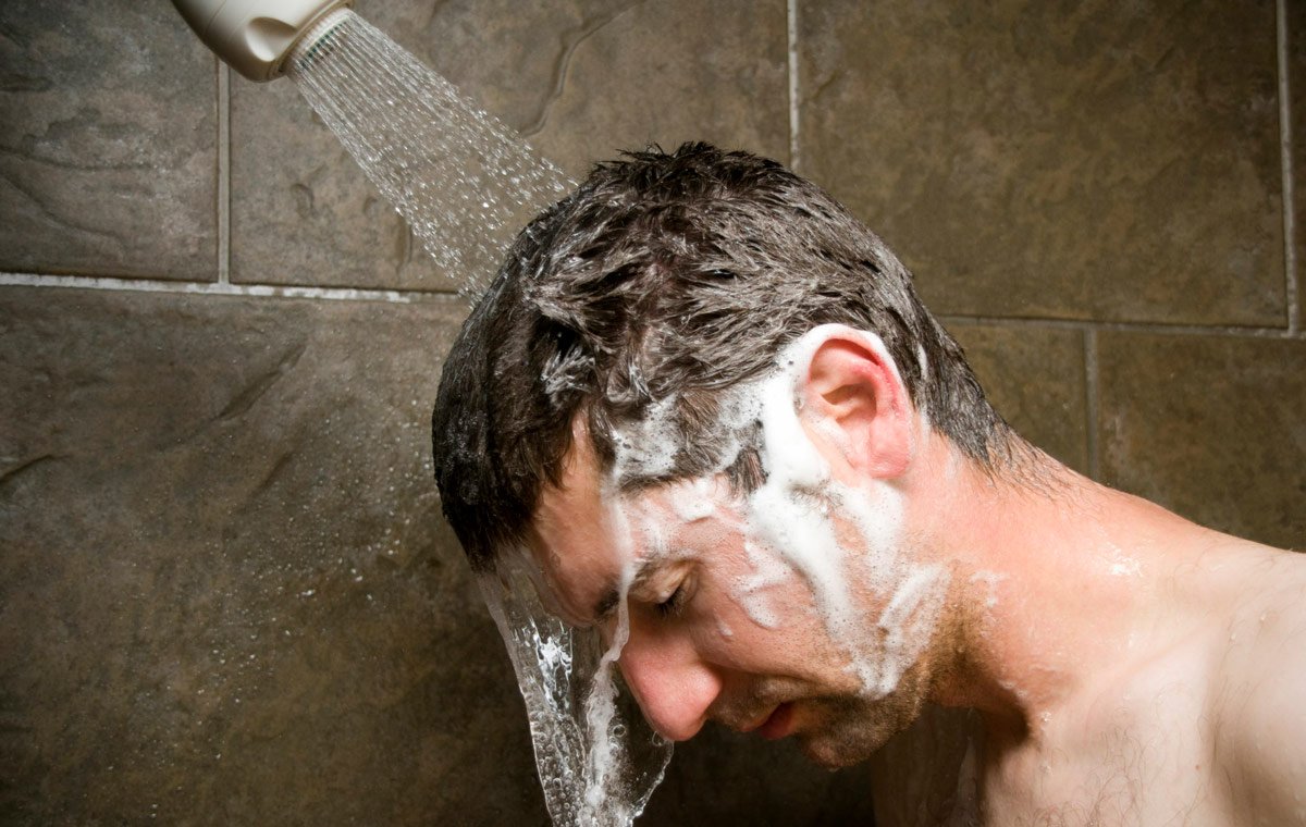 یک مرد جوان که زیر دوش شامپوهای روی سرش را می‌شوید