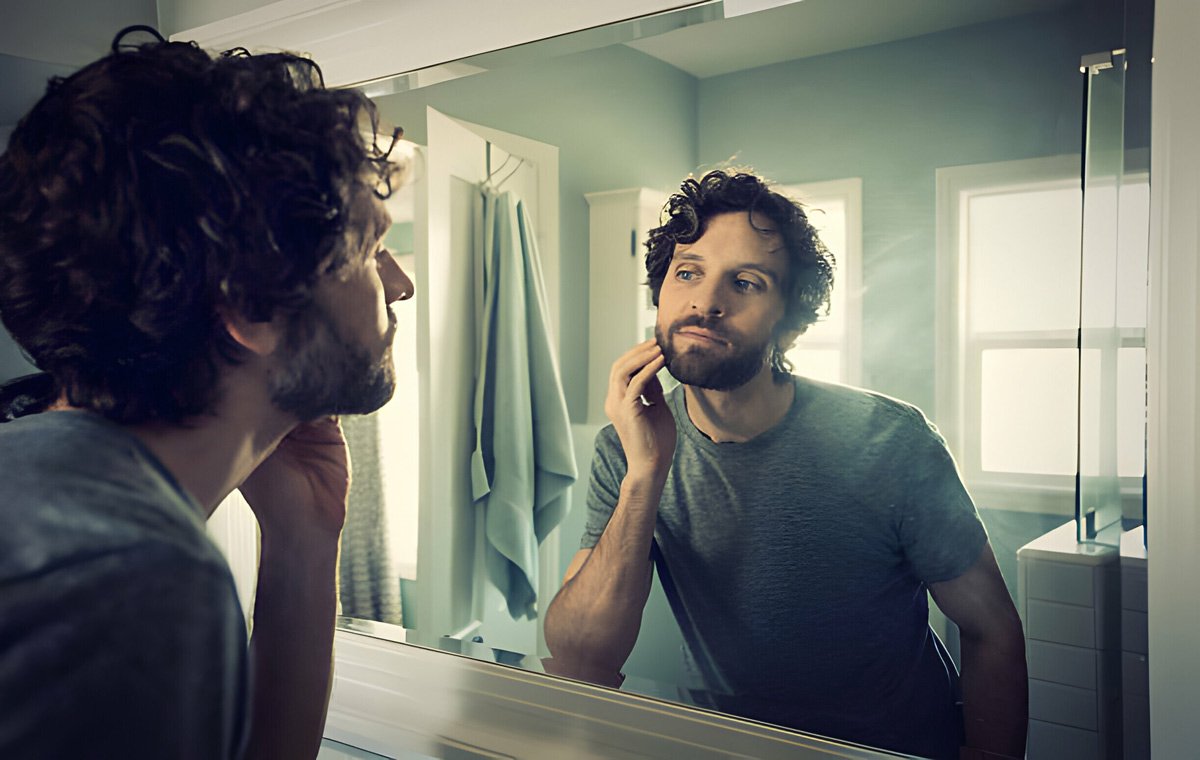 یک مرد جوان که در آینه به موهای صورت خود نگاه می‌کند