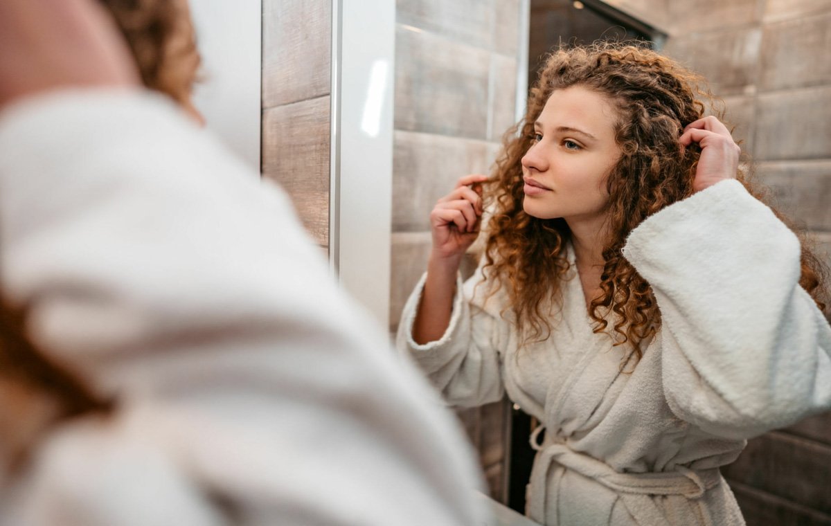 یک زن جوان که در آینه به موهای خود نگاه می‌کند