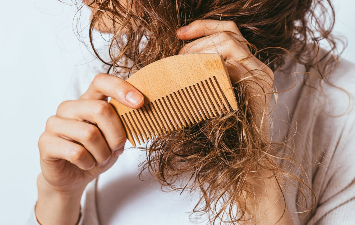 یک زن که از کرم مو برای سشوار استفاده کرده و در حال شانه کردن موهایش است