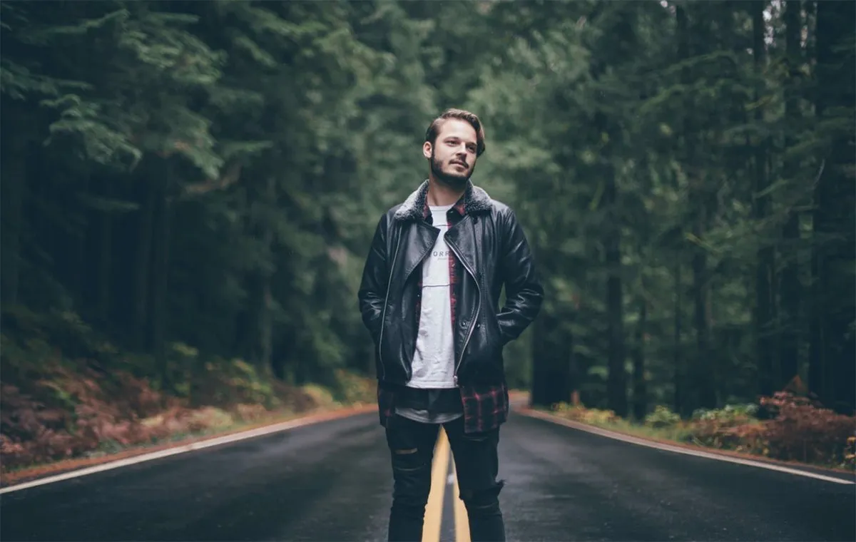 مردی با کت چرم ایستاده در یک جاده حنگلی