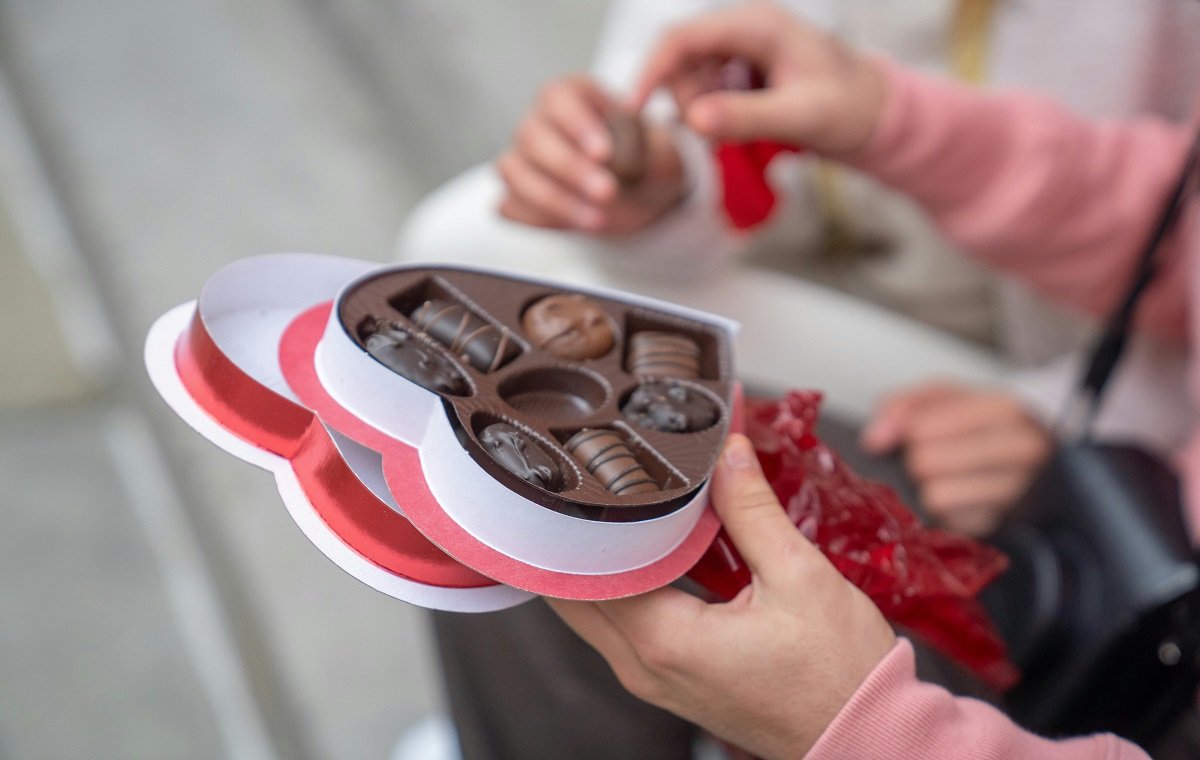 یک بسته قلب شکل پراز شکلات تلخ و شکلات قهوه ا و شکلات ولنتاین دست دو نفر است