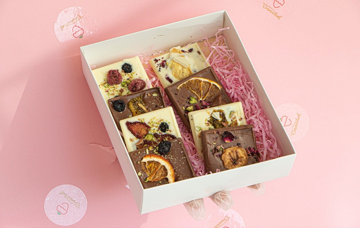 یک جعبه پر از شکلات ولنتاین و شکلات پر مغز و شکلات با تزئین میوه در تصویر است
