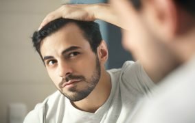 مرد جوان به خط رویش موی خود در آینه نگاه می‌کند