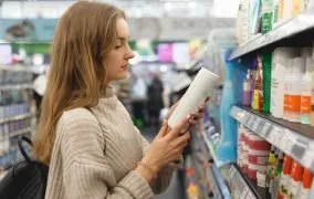 یک زن جوان در فروشگاه که ترکیبات روی شامپو ضد شوره را می‌خواند