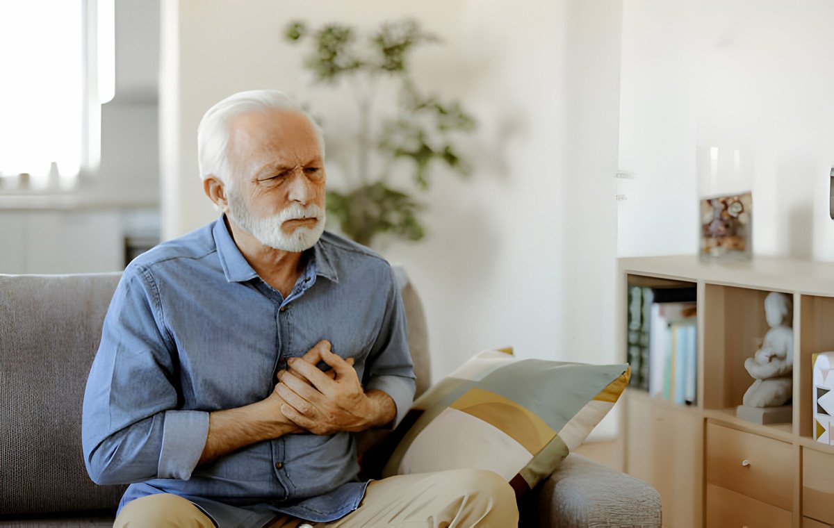 یک مرد سالمند روی مبل نشسته و با دست قلب خود را گرفته است