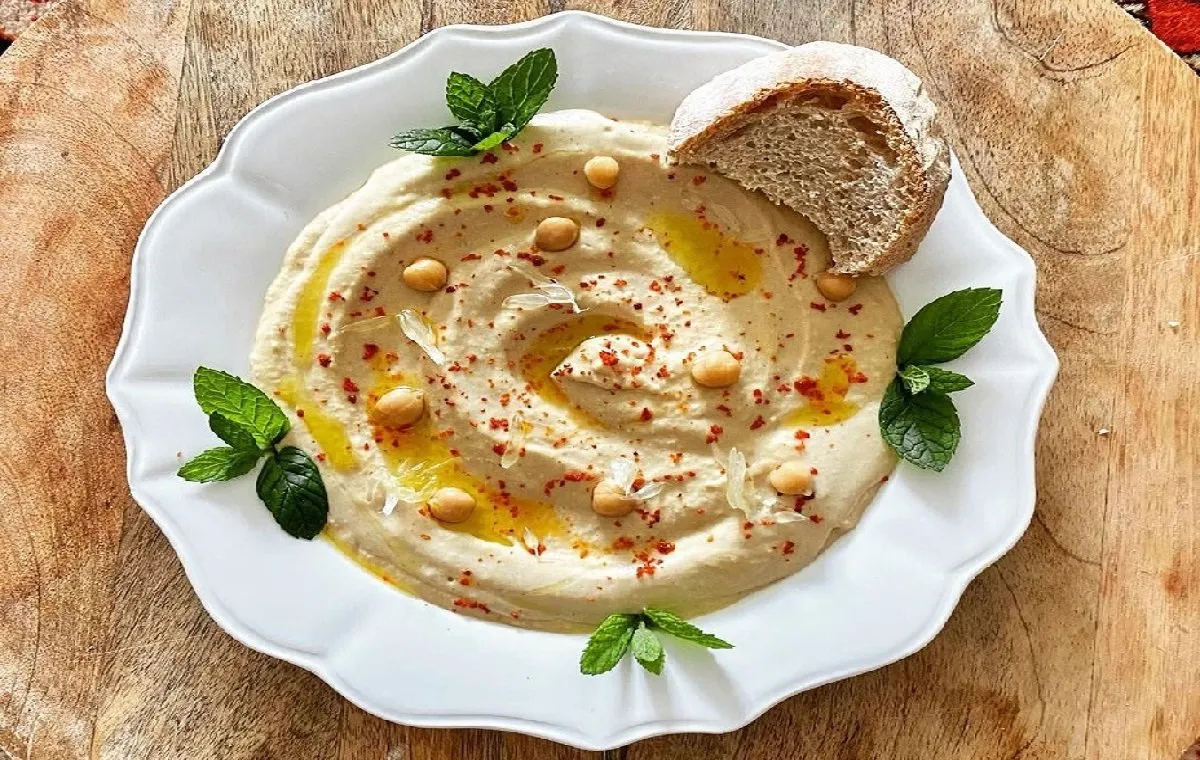 یک ظرف حمص لبنانی (نخود و سیر و ارده) با روغن زیتون که غذای ساده برای دورهمی های دوستانه است روی میز است