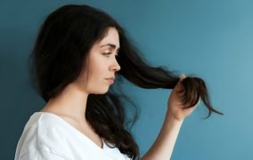 یک زن جوان یک دسته از موهای خود را در دست دارد و به آن‌ها نگاه می‌کند