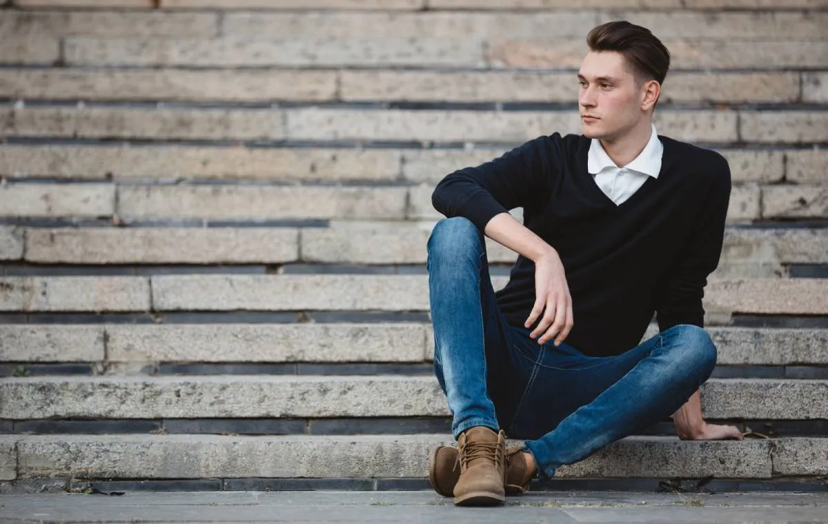 مردی جواین با شلوار جین روی پله نشسته است