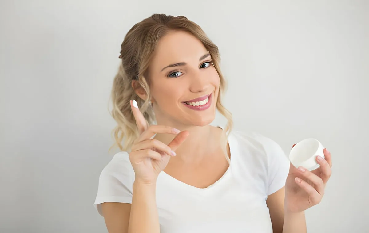 یک زن جوان که یک قوطی کرم در دست دارد و لبخند می‌زند