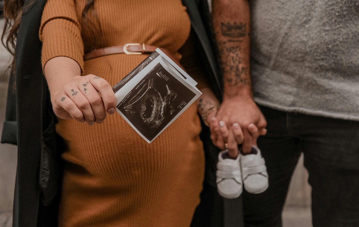یک خانم باردار در تصویر با عکس سونوگرافی و دست در دست همسرش است