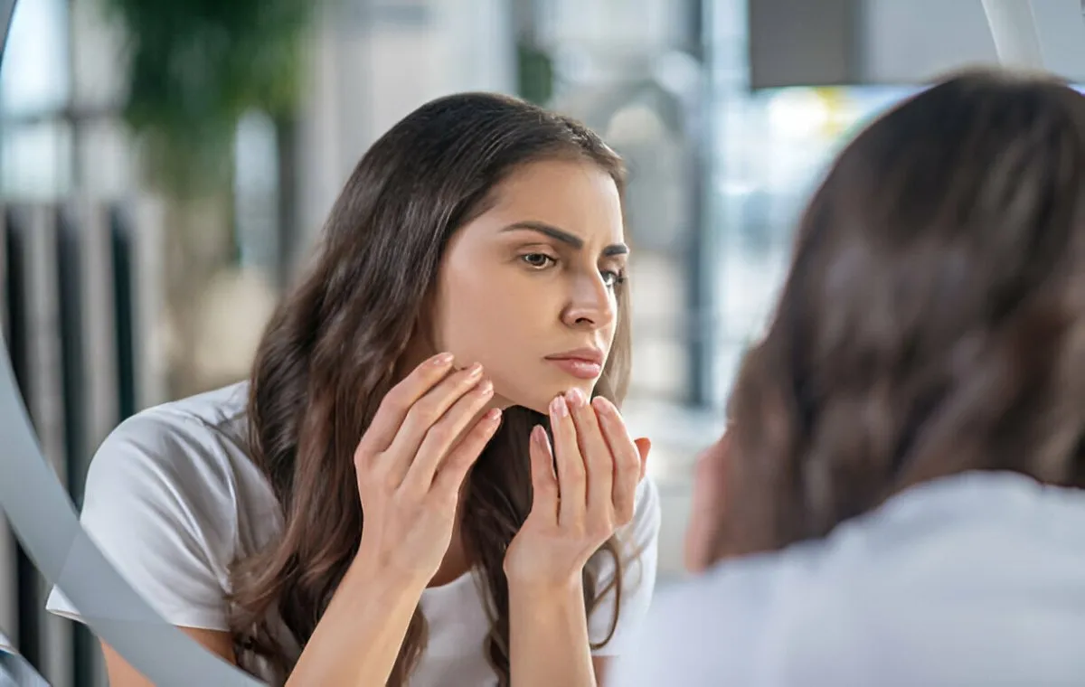 زن جوان در آینه به صورت خود نگاه میکند