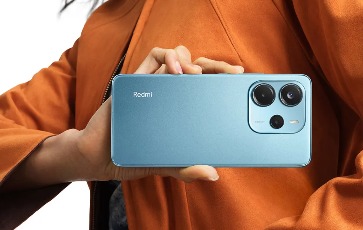 دختری با لباس نارنجی که گوشی آبی‌رنگ ردمی نوت ۱۴ را به‌صورت افقی در دست دارد و پشت گوشی به سمت ما است